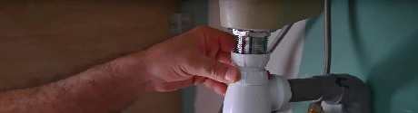 Mains manipulant les raccords de tuyauterie sous un lavabo
