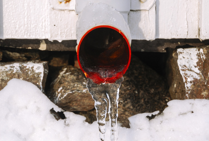 Eau s'écoulant d'un tuyau rouge dans la neige en hiver