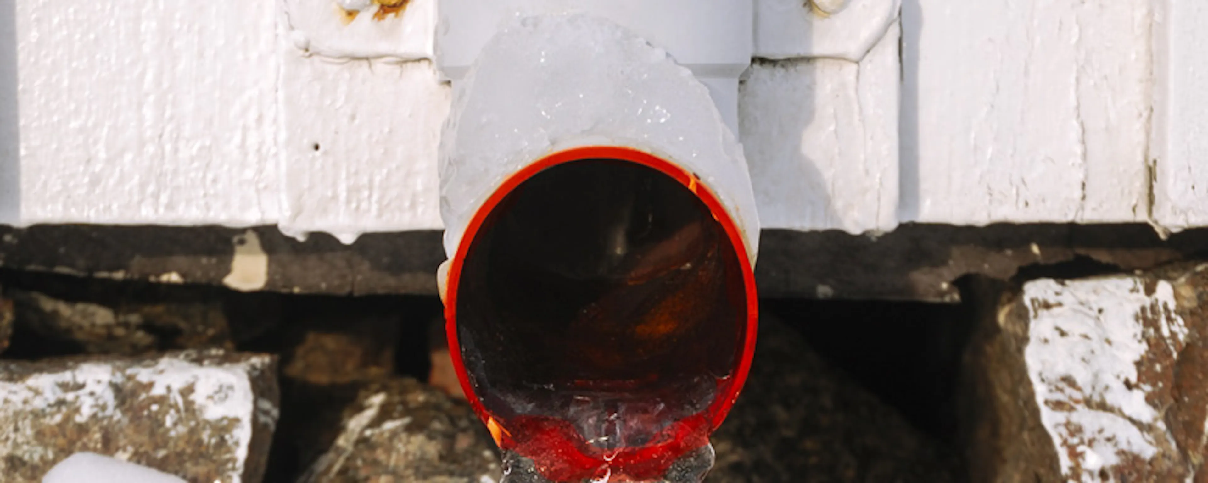 Eau s'écoulant d'un tuyau rouge dans la neige en hiver