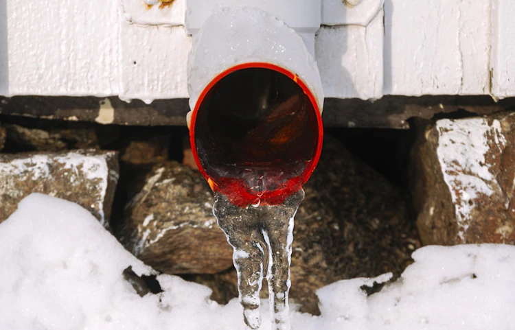 Eau s'écoulant d'un tuyau rouge dans la neige en hiver