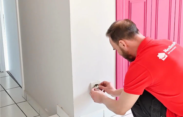 Technicien HomeServe accroupi installant un équipement au mur