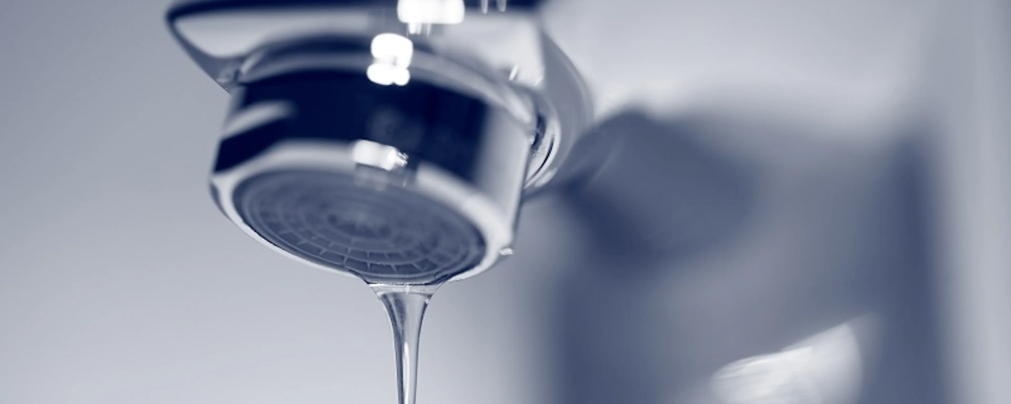 Robinet chromé avec une goutte d'eau qui tombe, fond flou