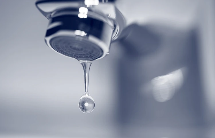 Robinet chromé avec une goutte d'eau qui tombe, fond flou