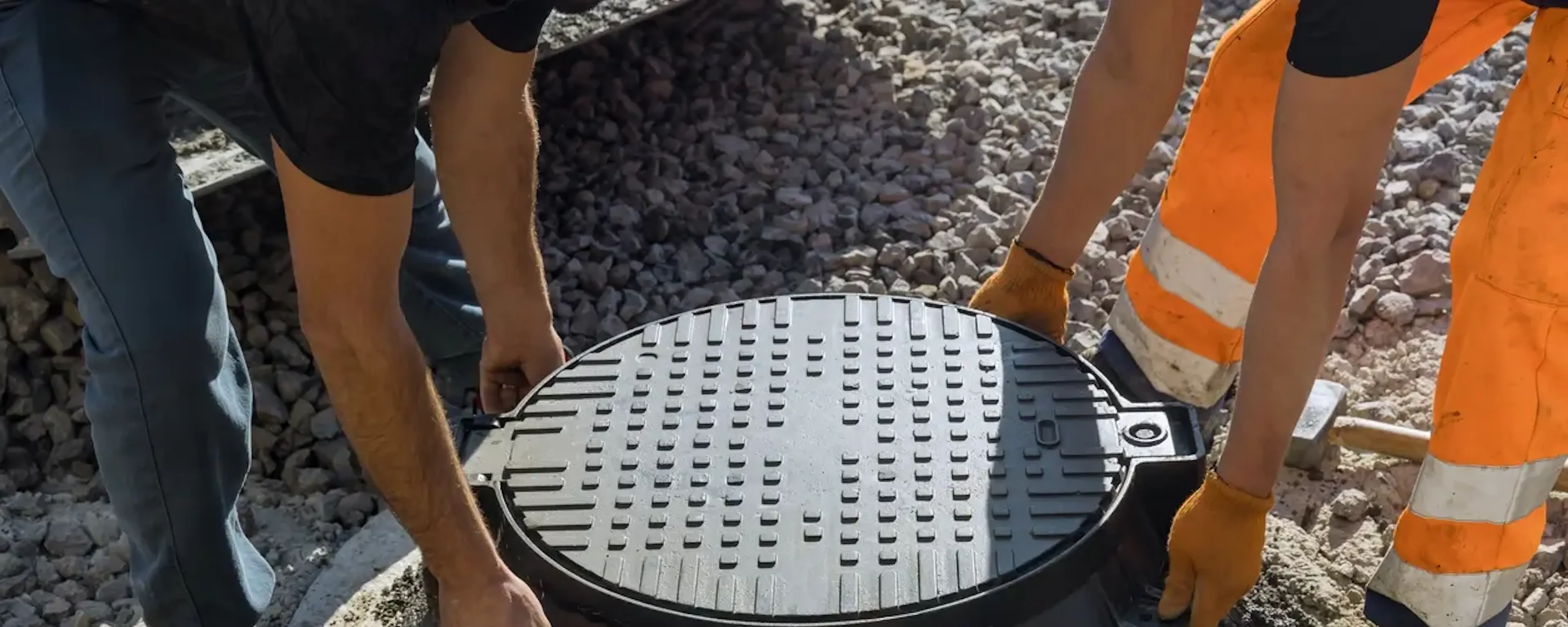 Deux ouvriers posant un couvercle de regard en fonte sur chantier