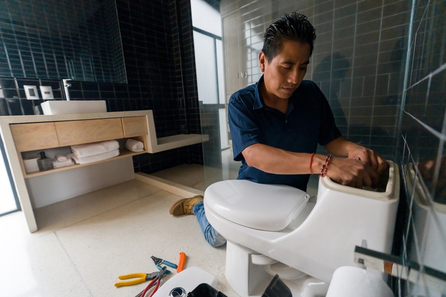 Plombier à genoux réparant les toilettes dans une salle de bain moderne