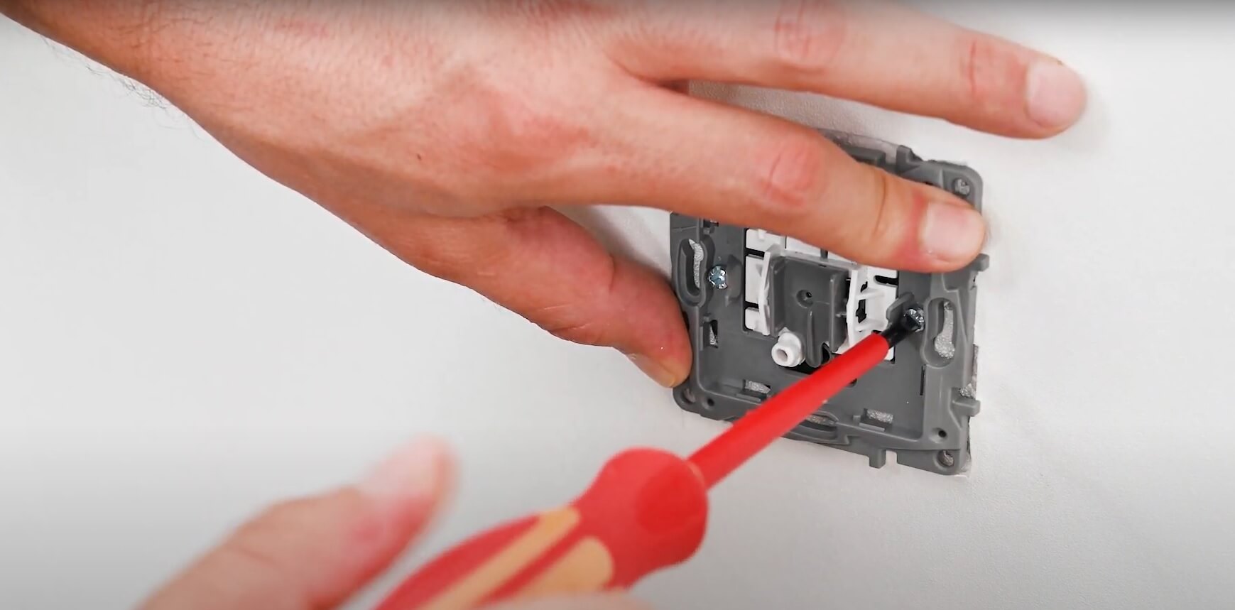 Main fixant le mécanisme d'un interrupteur avec un tournevis rouge