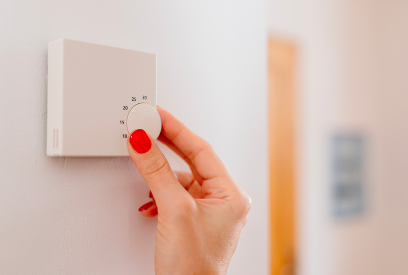 Main féminine réglant un thermostat mural blanc