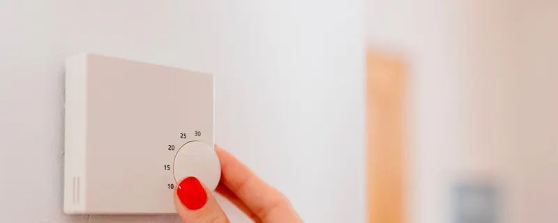 Main féminine réglant un thermostat mural blanc