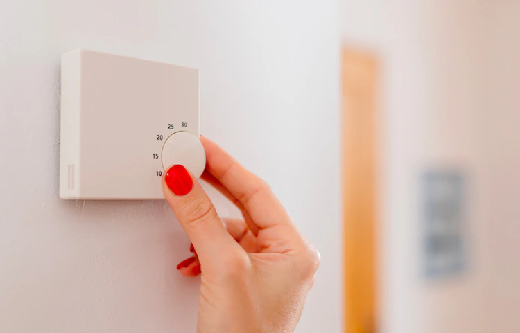 Main féminine réglant un thermostat mural blanc