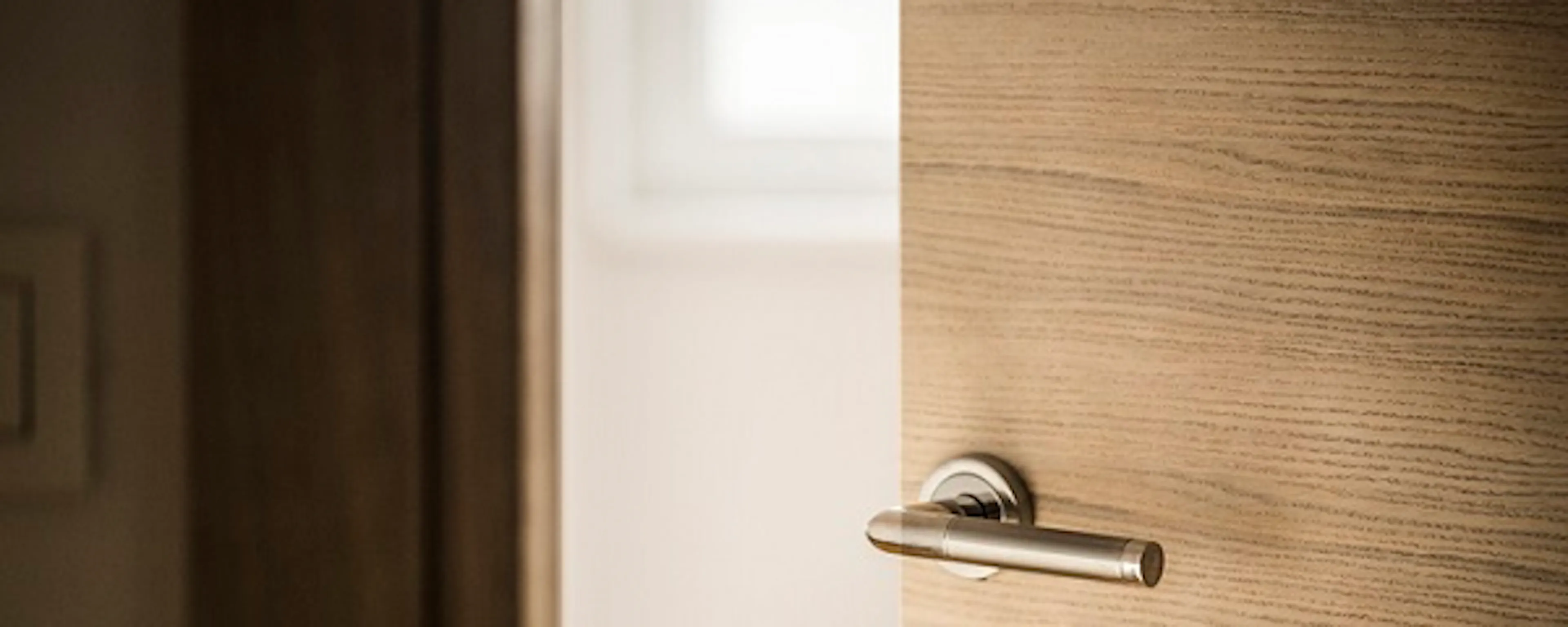 Porte en bois entrouverte avec une poignée et une serrure chromées