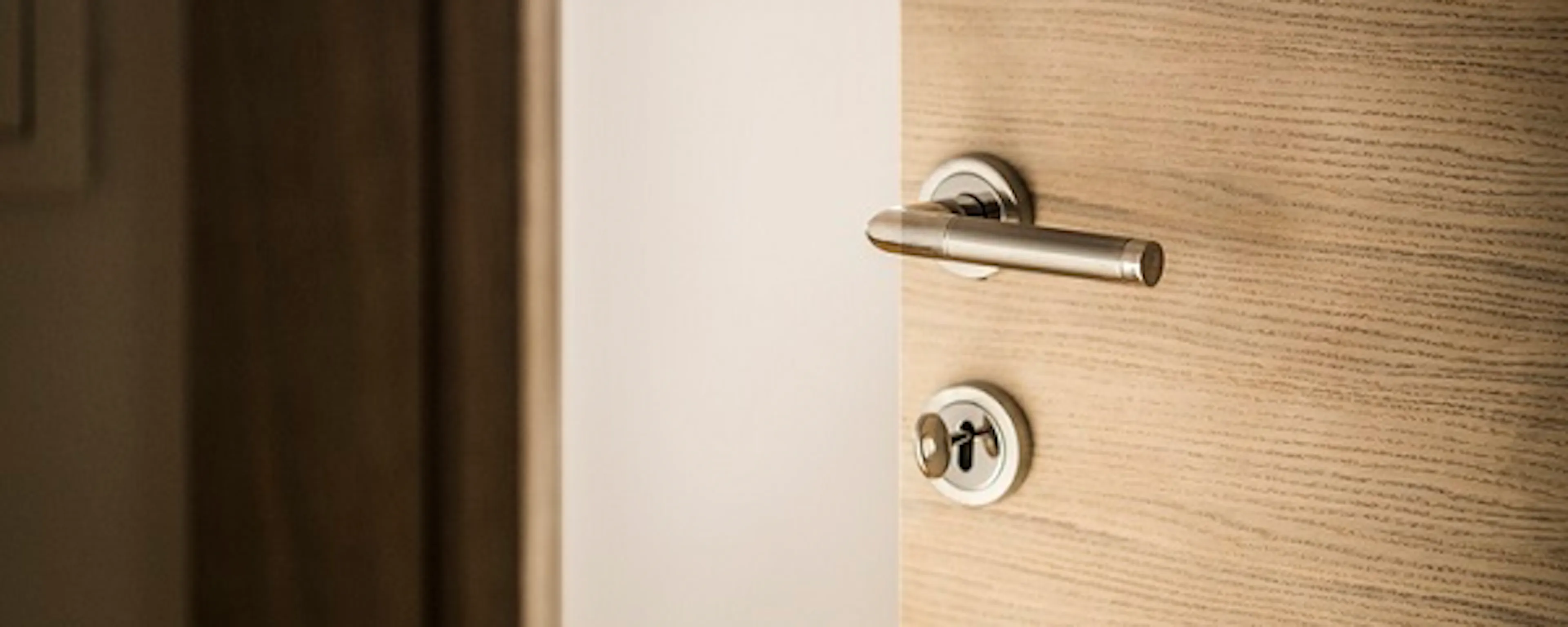 Porte en bois entrouverte avec une poignée et une serrure chromées