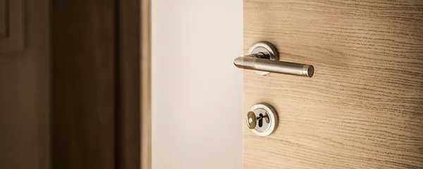 Porte en bois entrouverte avec une poignée et une serrure chromées