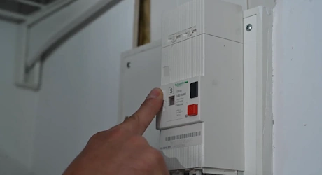 Doigt appuyant sur un bouton de disjoncteur principal dans un couloir