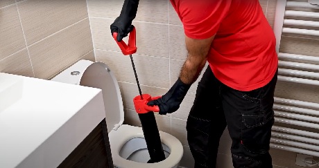 Plombier en rouge débouchant des WC avec un furet électrique