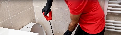 Plombier en rouge débouchant des WC avec un furet électrique