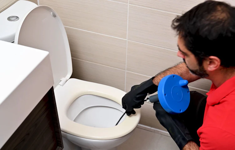Technicien utilisant un furet pour déboucher des toilettes