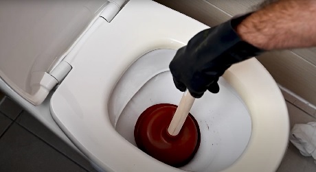 Main gantée utilisant une ventouse pour déboucher des toilettes