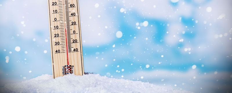Thermomètre en bois posé dans la neige sous un ciel hivernal