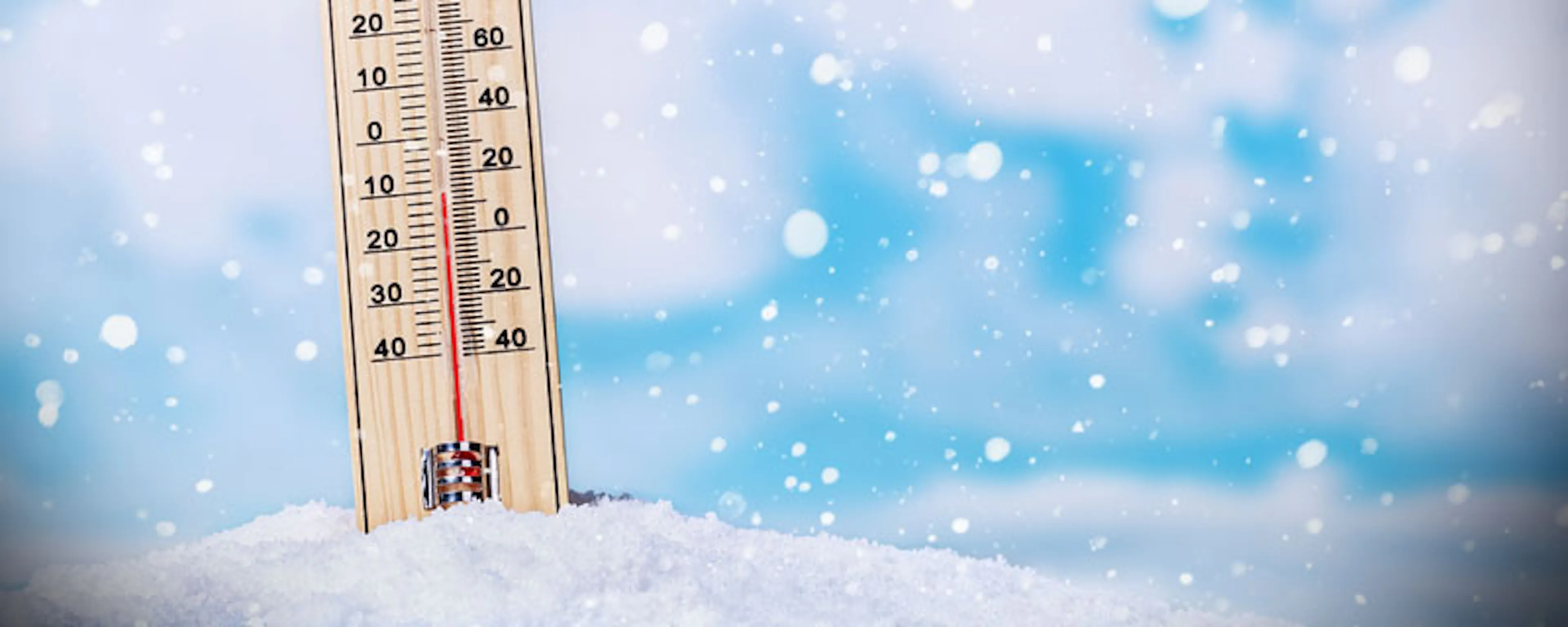 Thermomètre en bois posé dans la neige sous un ciel hivernal