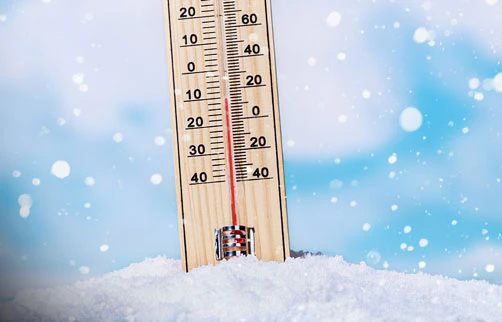 Thermomètre en bois posé dans la neige sous un ciel hivernal