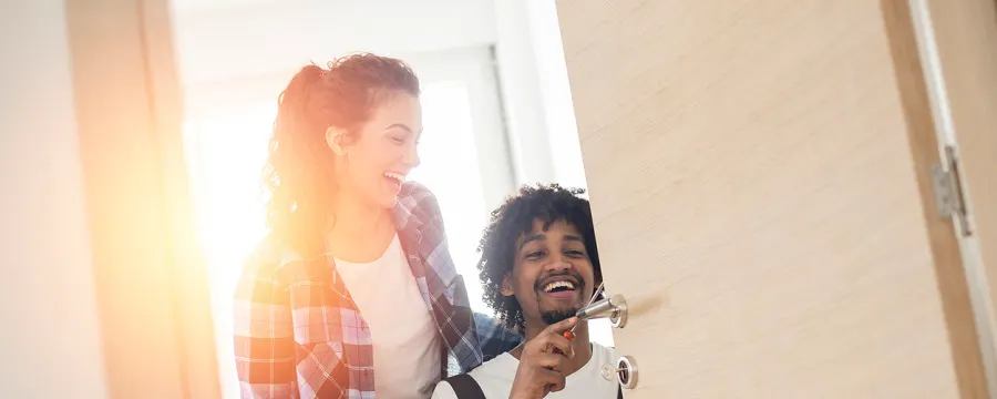 Couple souriant devant une porte d'entrée, homme tenant des clés