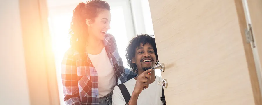 Couple souriant devant une porte d'entrée, homme tenant des clés