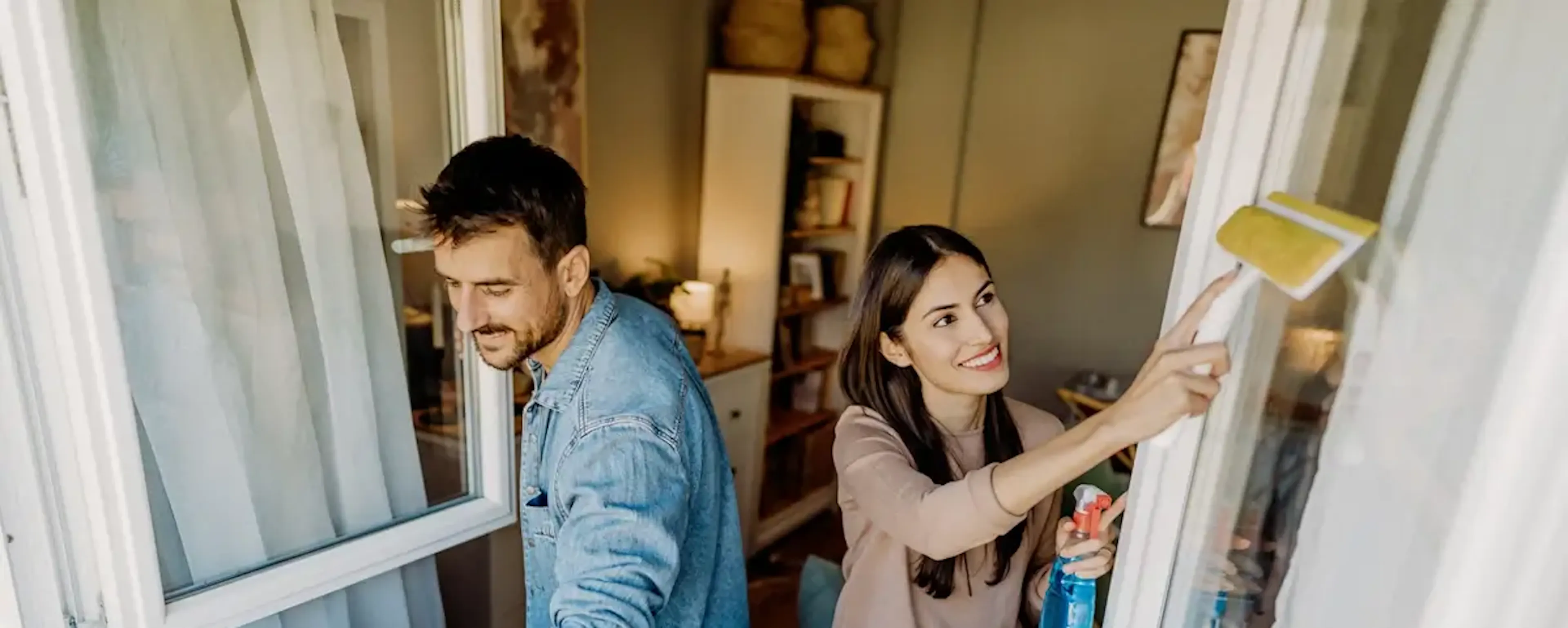 Couple nettoyant ensemble les vitres d'une fenêtre intérieure