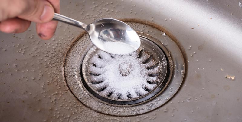 Main versant du bicarbonate de soude dans un siphon d'évier métallique