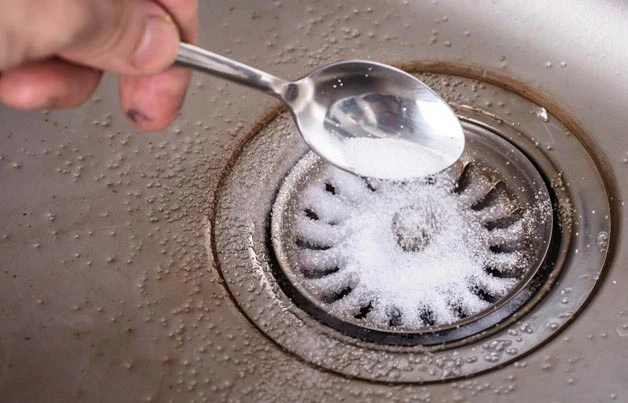 Main versant du bicarbonate de soude dans un siphon d'évier métallique