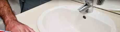 Main appliquant du silicone autour d'un lavabo blanc avec un pistolet à mastic