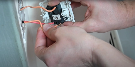 Mains raccordant des fils électriques orange sur un interrupteur encastré