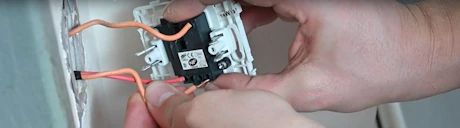 Mains raccordant des fils électriques orange sur un interrupteur encastré