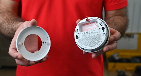 Technicien en rouge tenant le support et le corps d'un détecteur de fumée