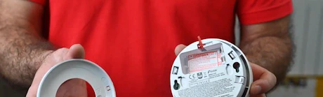 Technicien en rouge tenant le support et le corps d'un détecteur de fumée