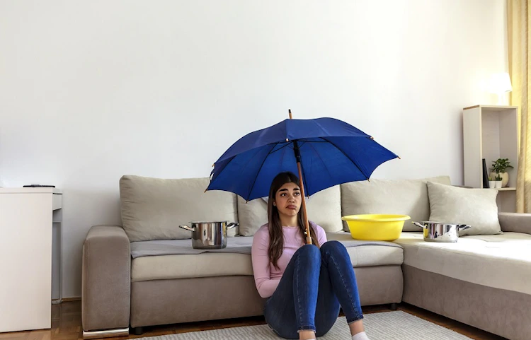 Femme assise sous un parapluie bleu dans un salon avec bassines
