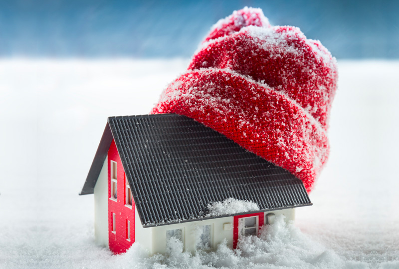 Maquette de maison portant un bonnet rouge posée dans la neige