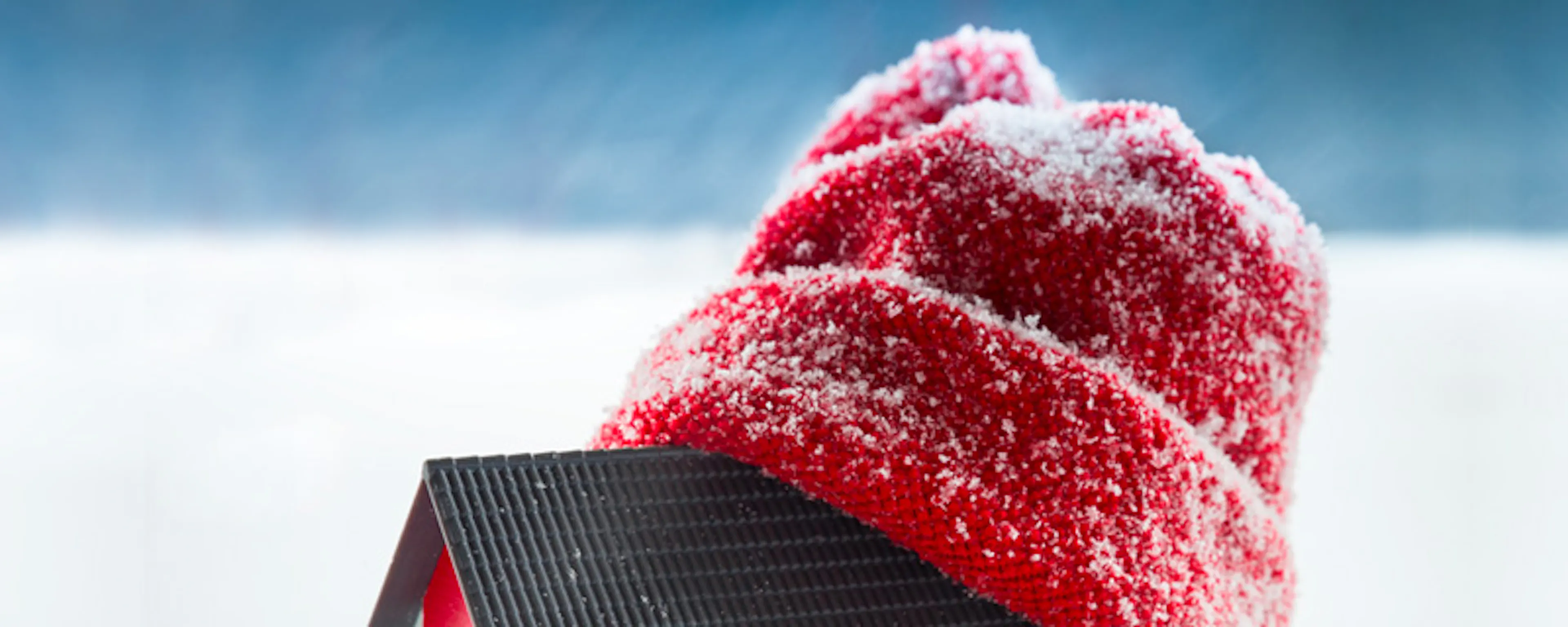 Maquette de maison portant un bonnet rouge posée dans la neige