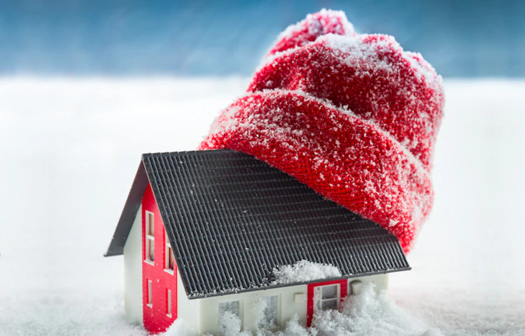 Maquette de maison portant un bonnet rouge posée dans la neige