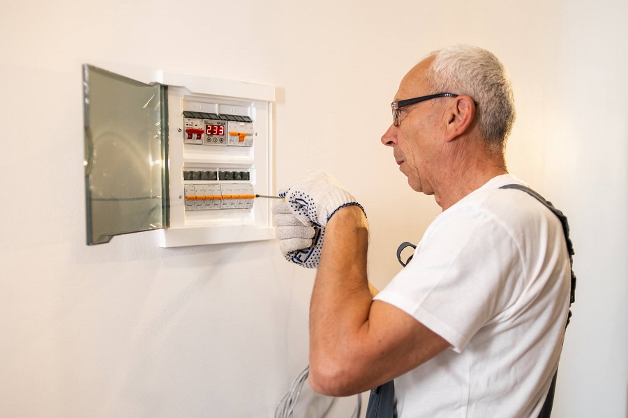 Homme âgé vérifiant un tableau électrique ouvert sur un mur blanc