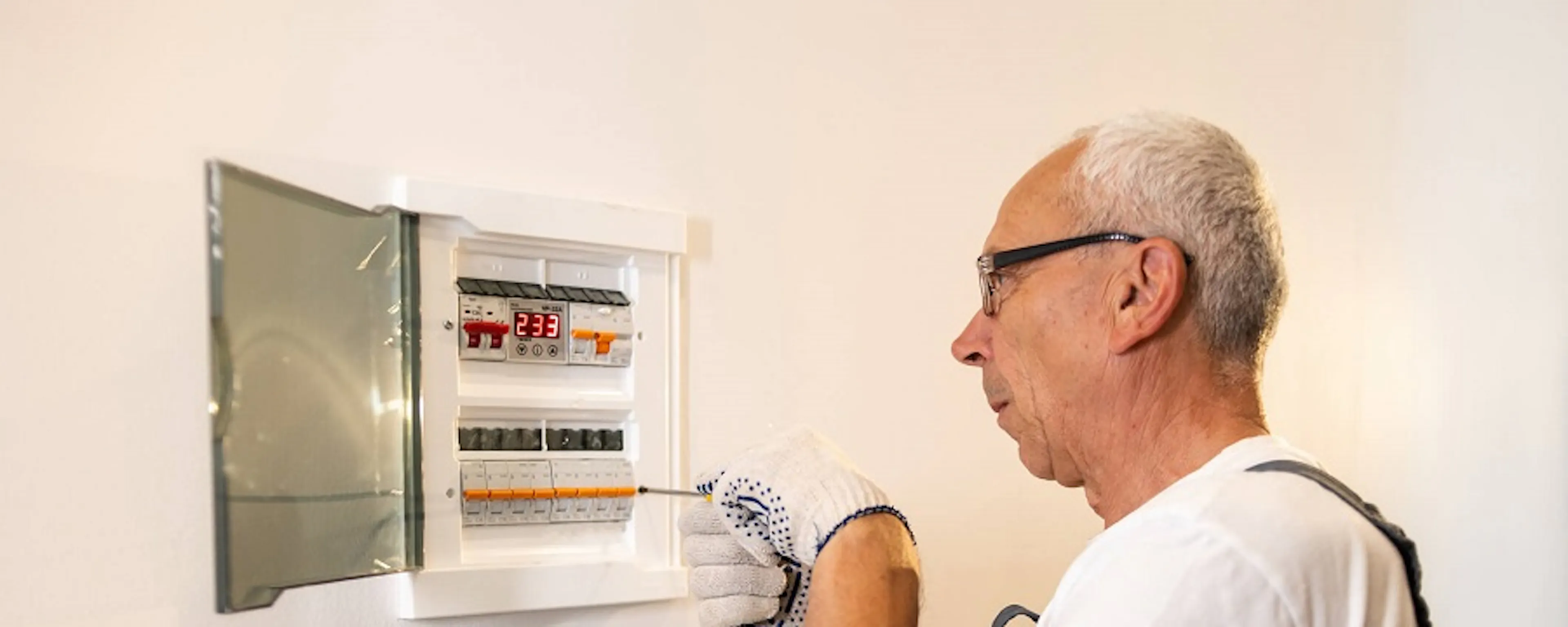 Homme âgé vérifiant un tableau électrique ouvert sur un mur blanc