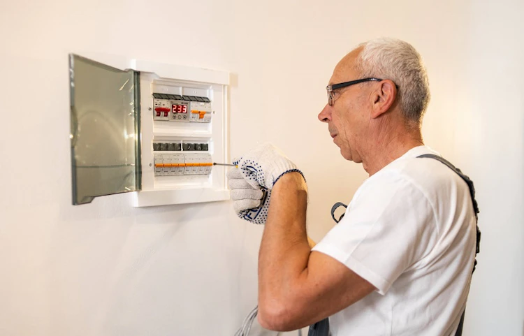 Homme âgé vérifiant un tableau électrique ouvert sur un mur blanc