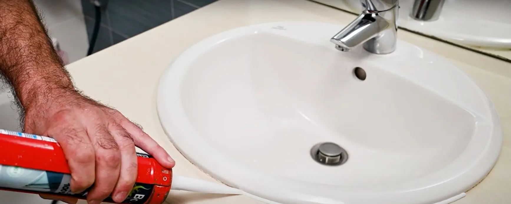 Main appliquant du mastic silicone autour du bord d'un lavabo blanc