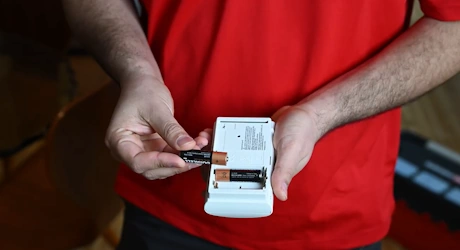 Mains en rouge insérant une pile dans un détecteur de fumée