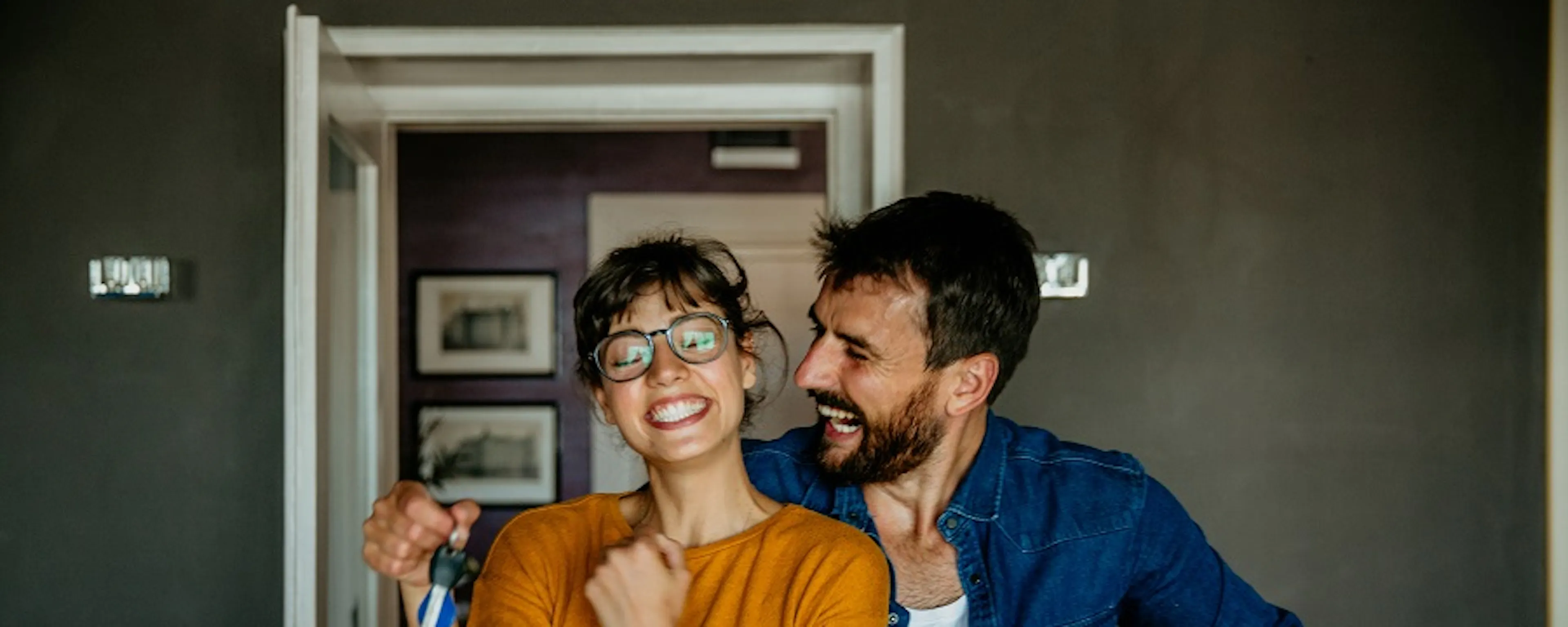 Couple souriant tenant des clés et un carton dans un appartement