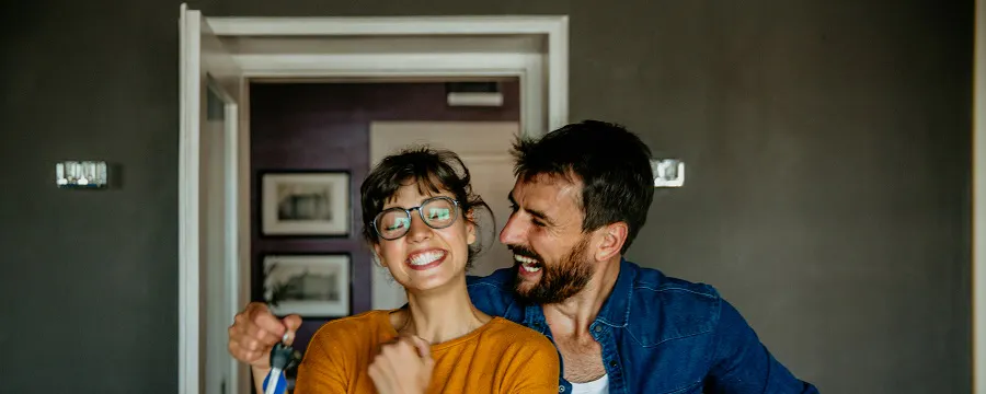 Couple souriant tenant des clés et un carton dans un appartement