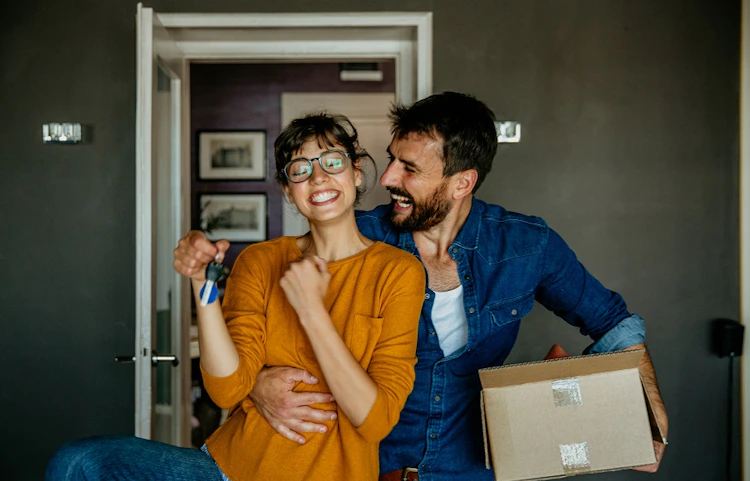 Couple souriant tenant des clés et un carton dans un appartement