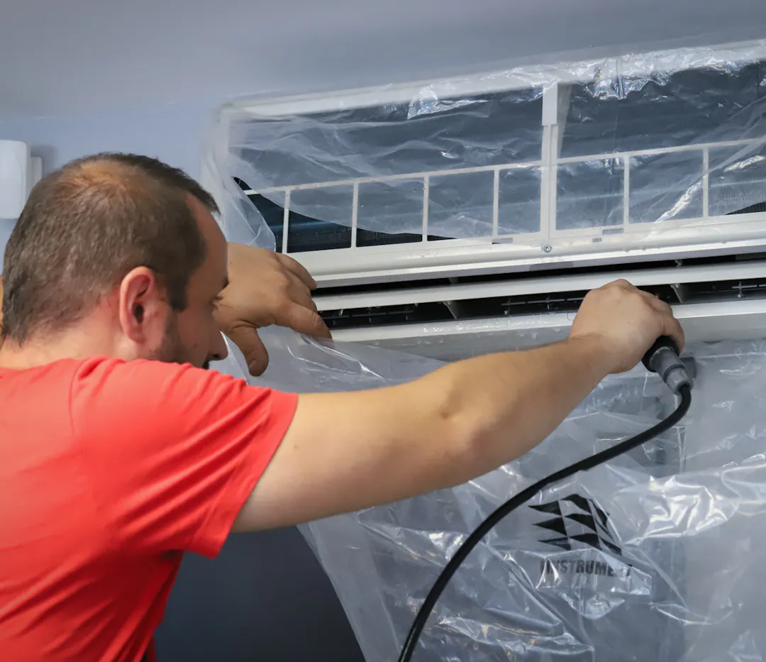 Un technicien de maintenance climatisation en train de nettoyer l'intérieur d'une unité de climatisation