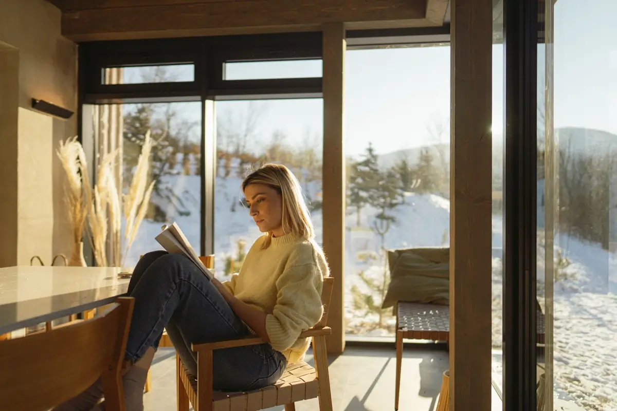 Femme lisant un livre près d'une grande fenêtre enneigée