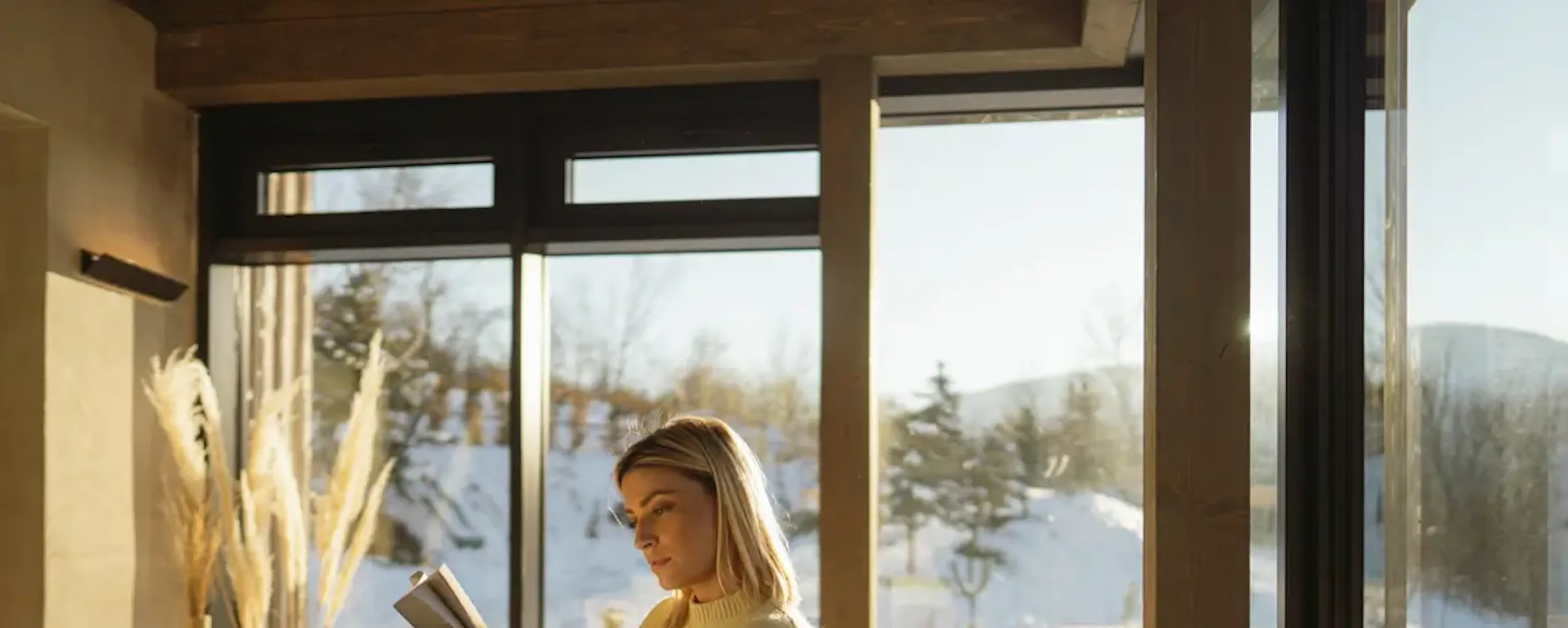 Femme lisant un livre près d'une grande fenêtre enneigée