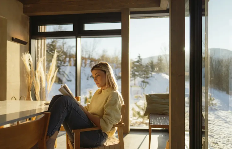 Femme lisant un livre près d'une grande fenêtre enneigée